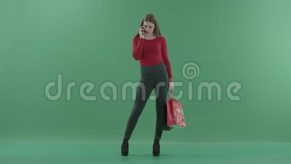 穿着休闲服的漂亮女人拿着购物袋在手机上说话她站在工作室里视频的预览图