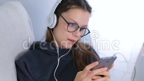 女人在智能手机上用耳机听音乐坐在扶手椅上唱一首歌视频的预览图