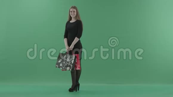漂亮的笑女人穿着黑色小裙子摆着购物袋她站在演播室里反对视频的预览图