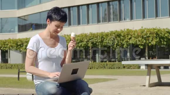 商务女性带着冰淇淋坐在办公楼前在电脑上工作视频的预览图