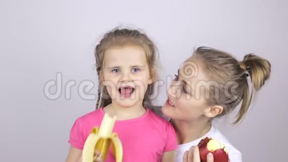 年轻的母亲带着女儿微笑着吃香蕉和苹果视频的预览图