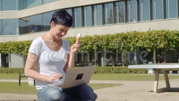 商务女性带着冰淇淋坐在办公楼前在电脑上工作视频的预览图