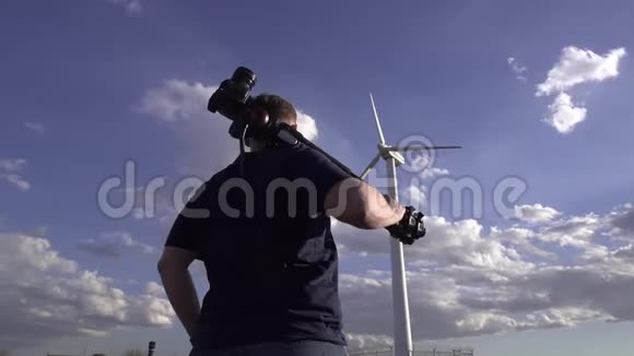 一个摄影师的肖像他在田野里看着远处一个美丽的风车肩上三脚架视频的预览图