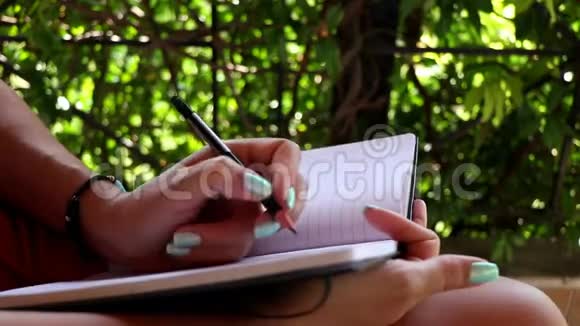 女人在阳台上的笔记本上写字女性在她的日记特写上做笔记视频的预览图