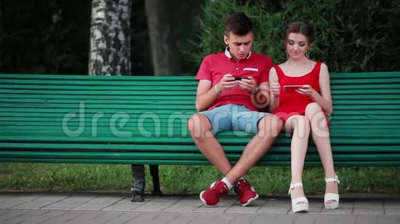 年轻人在公园里玩手机游戏在街上人们经过他们手里拿着智能手机视频的预览图