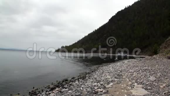 游艇靠近绿色的山地海岸和贝加尔湖光滑的石头视频的预览图