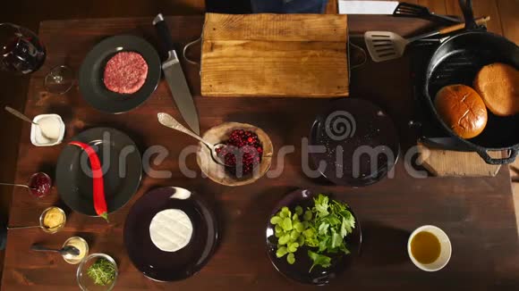 蓝色围裙的厨师站在餐桌旁桌上有制作汉堡包和煎包的配料视频的预览图