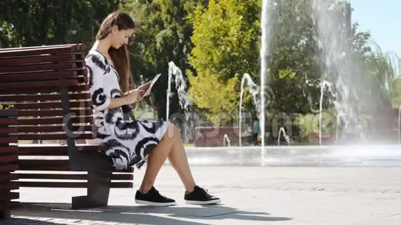 穿着连衣裙的年轻女商人坐在长凳上在写字板上讲话视频的预览图