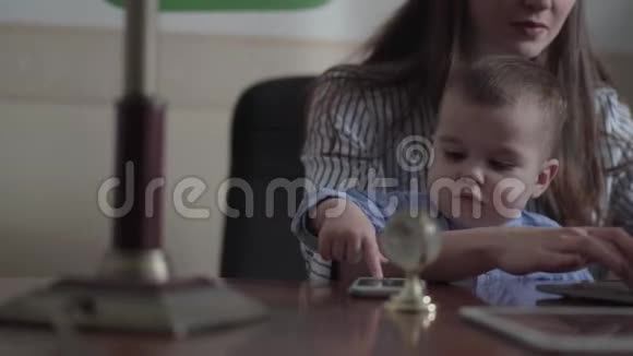 肖像可爱的年轻母亲和小儿子坐在桌子上的笔记本电脑在室内忙碌的年轻母亲在家工作视频的预览图
