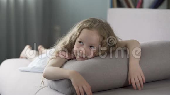 嬉戏的小女孩躺在家里的沙发上满脸笑容地等待着父母视频的预览图
