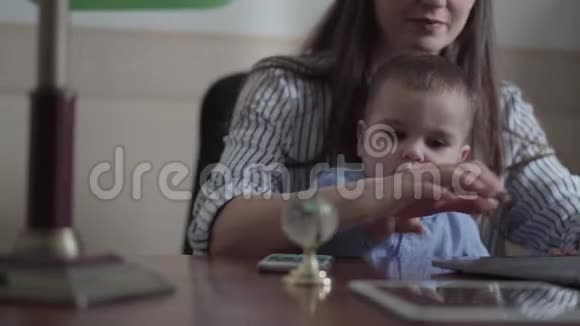 母亲和小儿子坐在室内桌子上的笔记本电脑的肖像忙碌的年轻母亲在家工作这就是视频的预览图