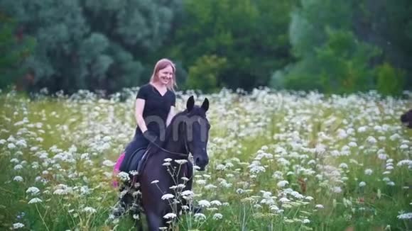 快乐的年轻女子骑在黑色的马背上在田野里开着花视频的预览图