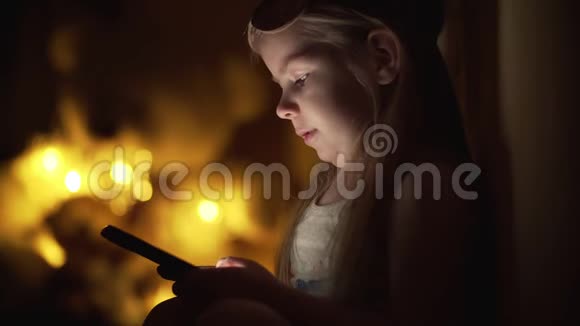 晚上可爱的小女孩在家里用智能手机女孩打字信息视频的预览图