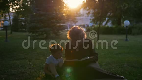 祖母在日落时分给坐在草地上的孙子读一本书视频的预览图