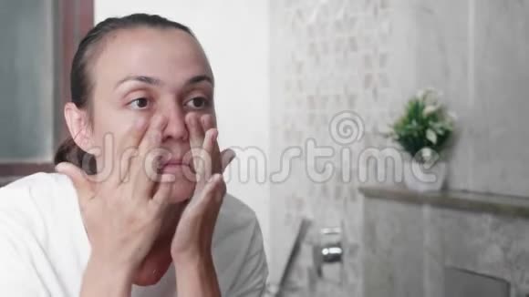 年轻女子正在脸上涂霜在浴室里做按摩动作视频的预览图