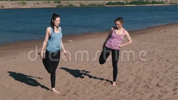 两个女人在日落时沿着河沙滩慢跑后做伸展运动视频的预览图