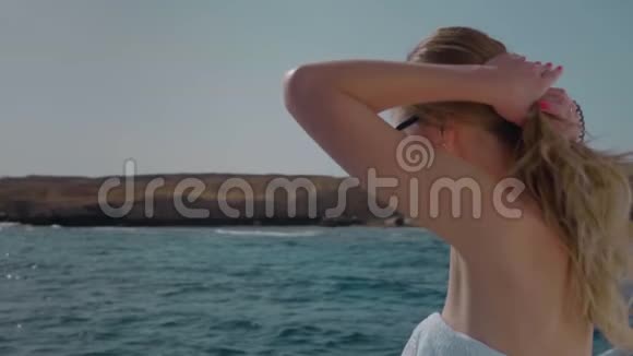 慢动作穿比基尼的金发美女在游艇上把头发扎成一个发髻大海背景上的玫瑰视频的预览图