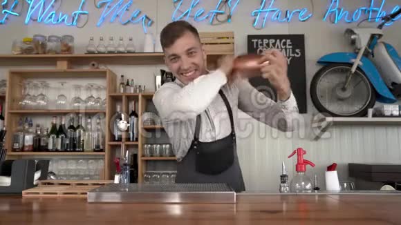 一位英俊的年轻酒保站在酒吧柜台前用鸡尾酒摇着一杯鸡尾酒视频的预览图