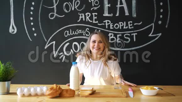 一个穿着睡衣的漂亮女人一件白色的t恤准备在厨房的家里吃早餐牛奶面包视频的预览图
