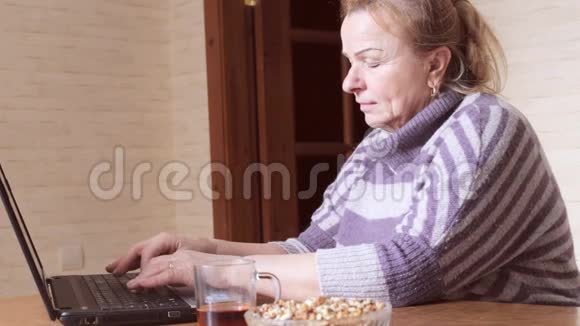 奶奶坐在厨房里在笔记本电脑后面聊天视频的预览图