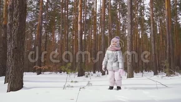 可爱的小女孩在冬天的森林里跳上雪地慢动作视频的预览图