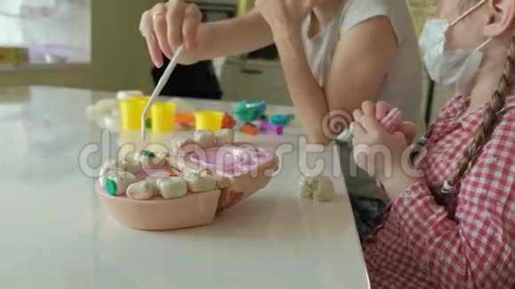 一个年轻的女人和一个女孩用塑料制成牙齿把牙齿插入玩具下巴做检查玩视频的预览图