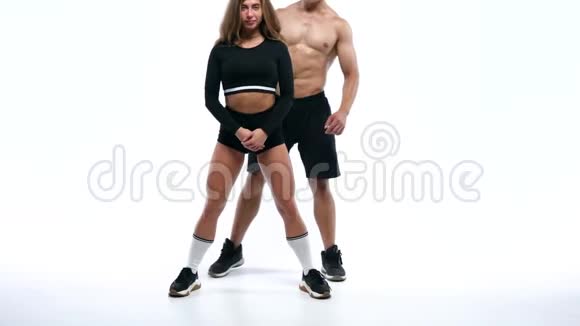 运动男把一个女孩放在肩膀上和她一起蹲在工作室的白色背景上视频的预览图