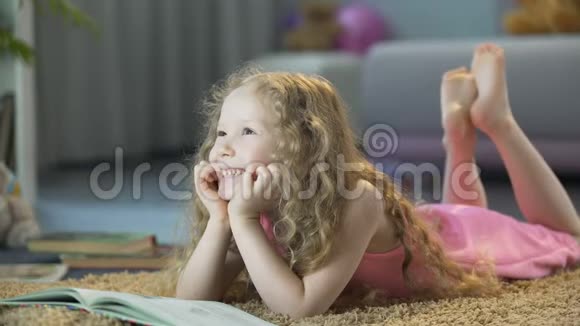 可爱的卷发女孩躺在家里柔软的地毯上微笑着快乐的孩子视频的预览图