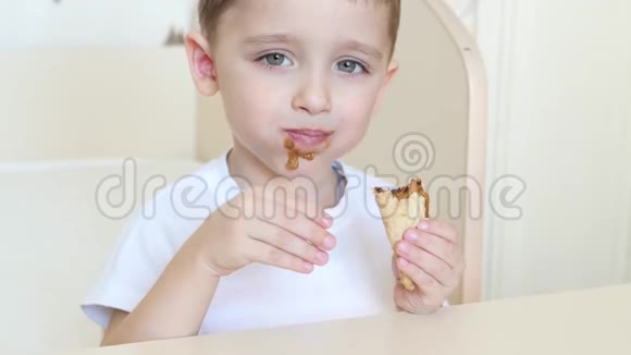 孩子坐在桌旁愉快地在华夫饼锥里吃着巧克力冰淇淋特写视频的预览图