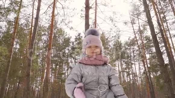 可爱的小女孩用手摇着摄像机和冬天的森林背景视频的预览图
