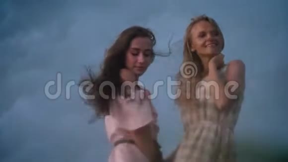 两个穿着裙子的年轻迷人的女孩在夏天的雨天里迎风欢笑自由的概念视频的预览图