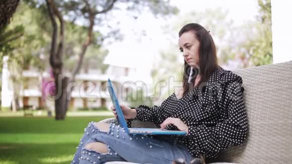 优雅的年轻女子坐在户外手提电脑远程工作女孩看着笔记本电脑屏幕在电脑上打字视频的预览图