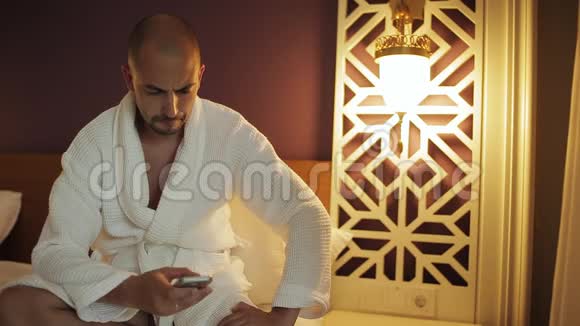 一个穿浴袍的男人晚上在酒店用电话视频的预览图