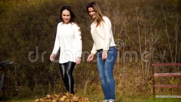 两个年轻女子将干枯的落叶踢向镜头两个女孩玩黄色的秋叶4k60fps视频的预览图