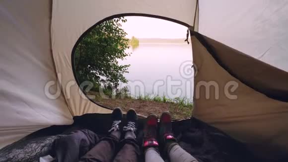 游客躺在帐篷里移动双脚让舞蹈动作变得有趣放松美丽的湖或河景是视频的预览图