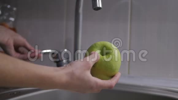 女人的手在水龙头下洗绿苹果一位年轻的家庭主妇在厨房里用水洗鲜绿苹果视频的预览图