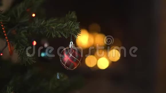 一个玻璃玩具挂在装饰的圣诞树上背景是闪烁的灯光和燃烧的壁炉视频的预览图