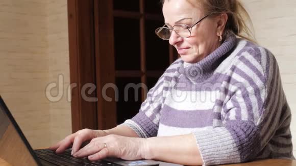 祖母坐在桌旁用笔记本电脑工作奶奶带电脑视频的预览图