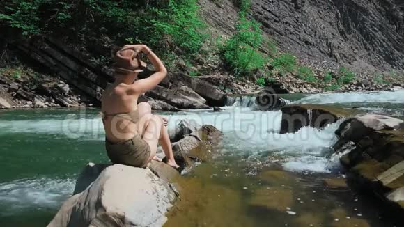 瑞士一条山河的岸边坐在岩石上的年轻女子脱下他的帽子披散他的长发视频的预览图