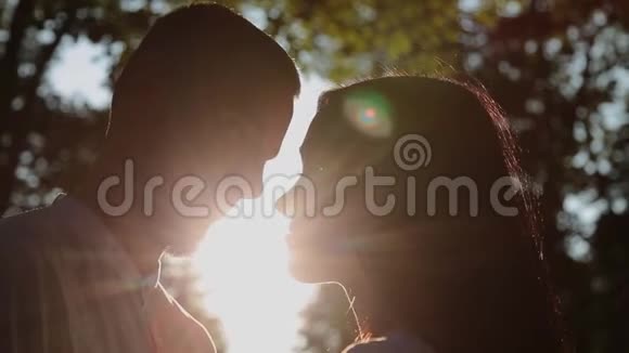 一对相爱的夫妇在日落的背景下拥抱和亲吻阳光穿过他们的脸视频的预览图