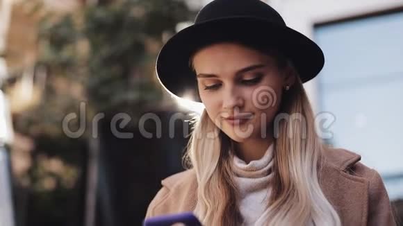 身穿外套戴着帽子的年轻女商人站在城市商业中心附近通过智能手机平板电脑进行交流视频的预览图