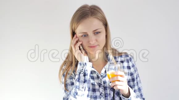年轻女子喝着一杯橙汁在智能手机上聊天视频的预览图