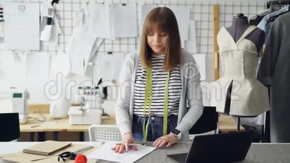 美丽的时装设计师正在为她的新衣服收集和使用笔记本电脑绘制服装草图光线视频的预览图