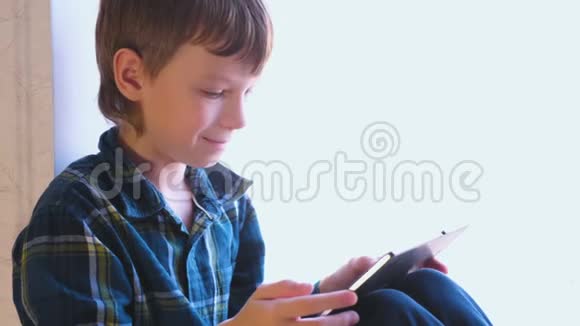 男孩正坐在窗台上玩平板电脑游戏视频的预览图