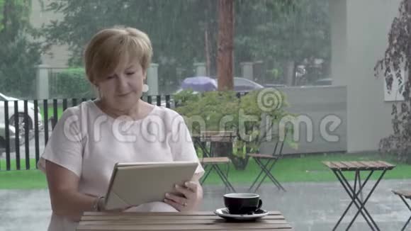 一位迷人的老妇人看着平板电脑打字坐在夏天的露台上视频的预览图