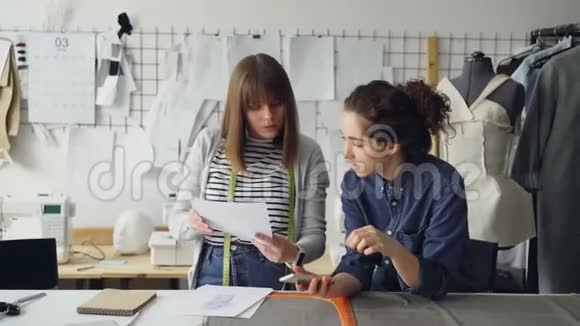 创意服装制造商正在使用智能手机和看服装草图同时在尼斯工作室工作傻瓜缝纫视频的预览图