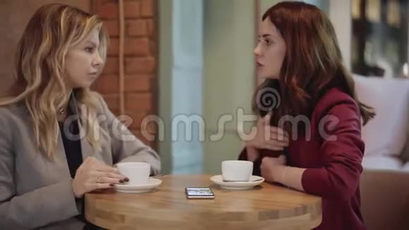 两个年轻女人在咖啡馆里聊天看着智能手机上的照片视频的预览图