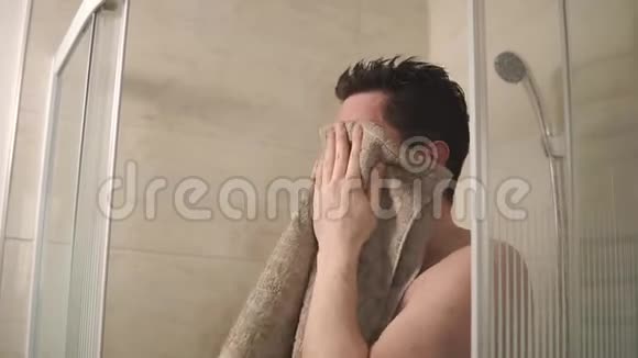 一个年轻人在浴室里用浴巾擦脸的肖像视频的预览图