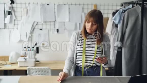 服装设计企业家正在检查纸张缝纫草稿和看智能手机她正在检查每一个切口视频的预览图