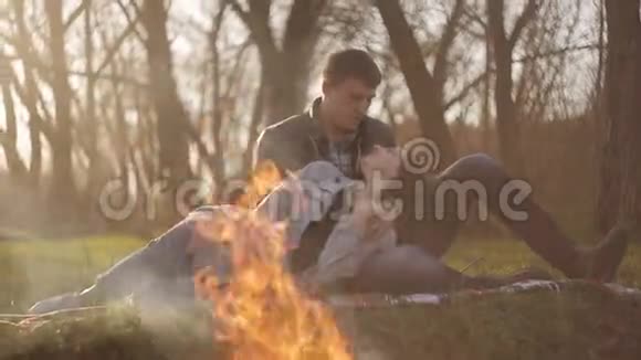 一对相爱的年轻夫妇在火边约会一个男人抱着一个女孩坐在火边的地毯上视频的预览图
